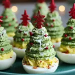 Festive Christmas deviled eggs decorated like mini Christmas trees with avocado filling and red sprinkles.